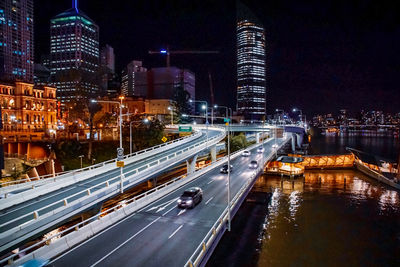 Illuminated bridge by buildings against sky at night