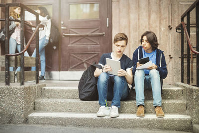 Male teenagers using digital tablet while sitting on steps outdoors