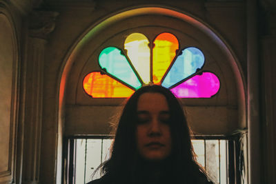 Portrait of young woman standing against illuminated window