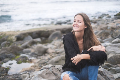 Smiling young woman on rock at beach