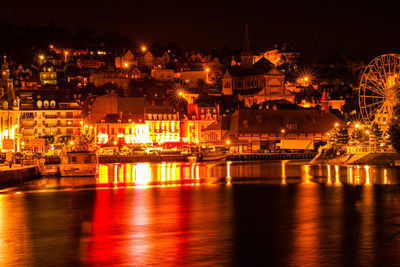 Illuminated city by river against sky at night