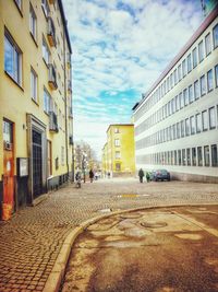 Empty road amidst buildings in city against sky