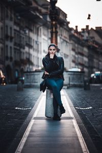 Full length portrait of young woman sitting in city