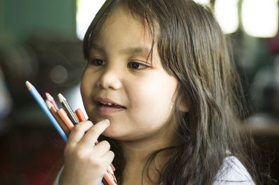 Thoughtful cute girl looking away while holding pencils