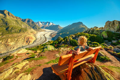 Woman sitting on bench against landscape