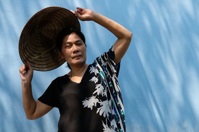 Mature woman wearing asian style conical hat against wall