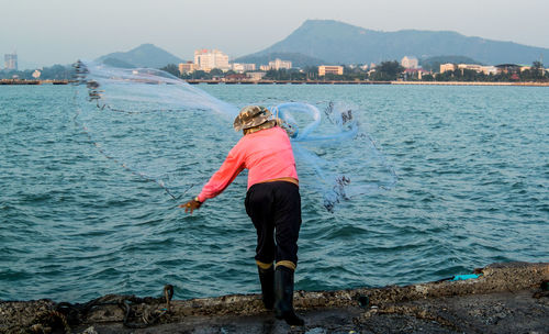 Full length rear view of man throwing fishing net in river