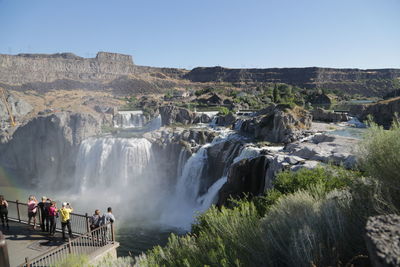 People at waterfall against clear sky