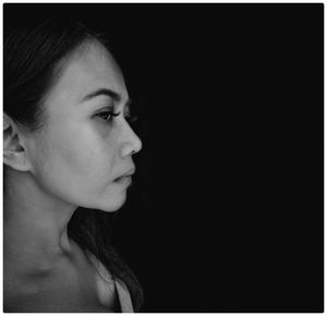 Close-up of woman looking away against black background