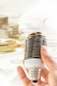 Cropped image of person holding electricity bulb made with stack of coins