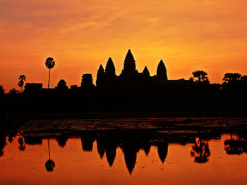 Silhouette temple by lake against sky during sunset