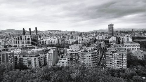 High angel view of buildings by trees against cloudy sky