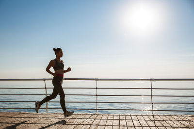 Woman jogging by sea against clear sky