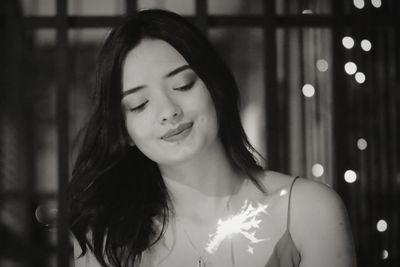 Young woman holding sparkler standing at home