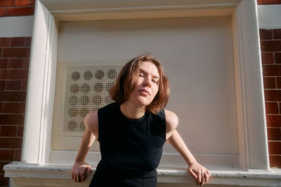 Portrait of young woman standing against wall