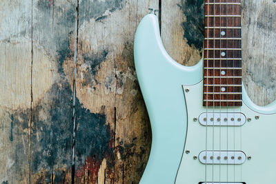 Detail of mint green electric guitar on a wood background.