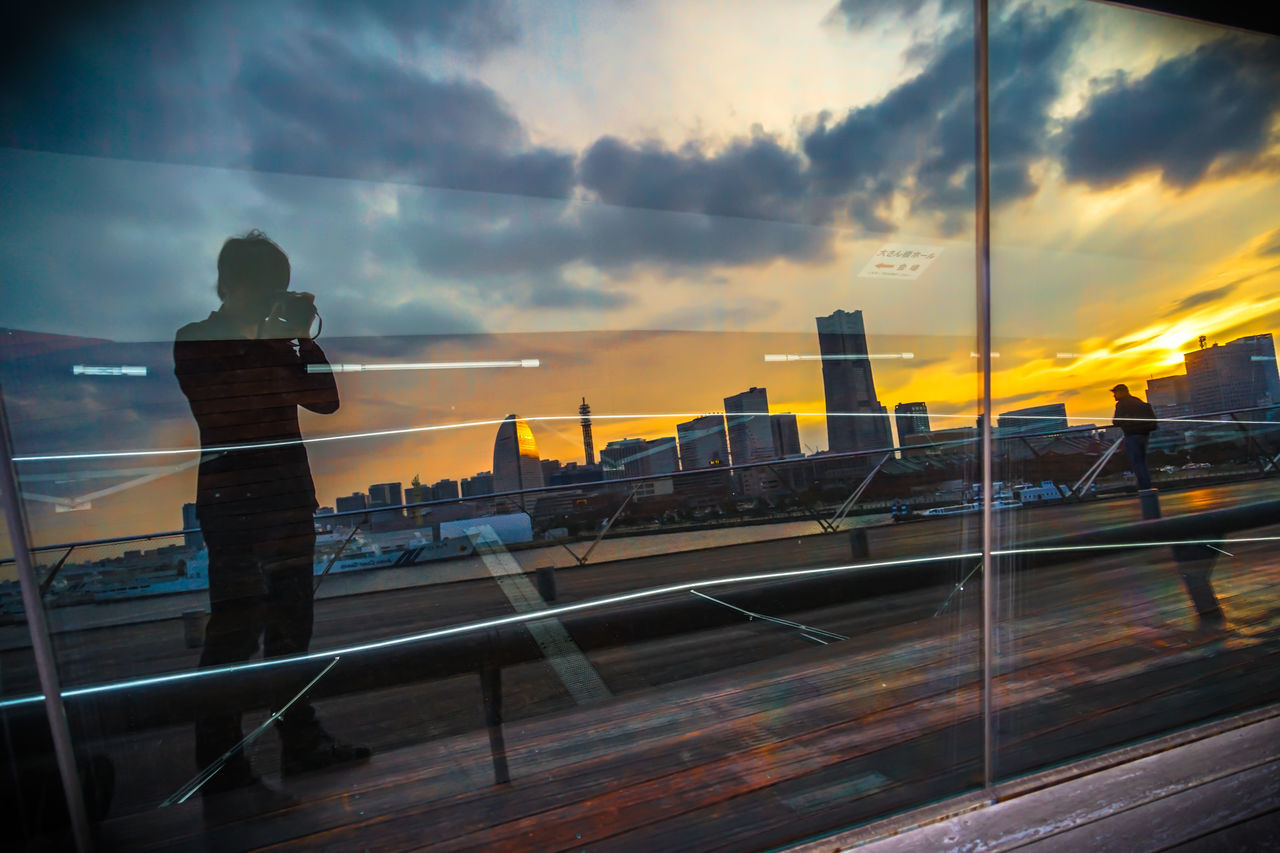 MAN STANDING BY RAILING AGAINST SKY DURING SUNSET