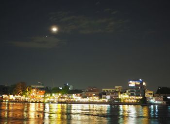 Illuminated city by sea against sky at night