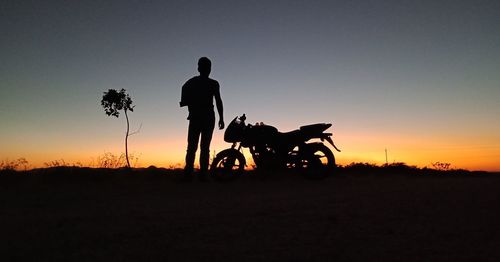 Silhouette man riding bicycle on field against sky during sunset
