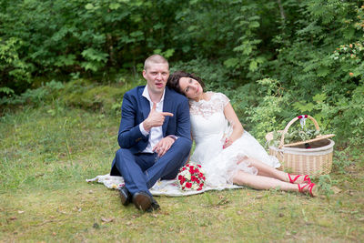 Portrait of bridegroom sitting with bride on field