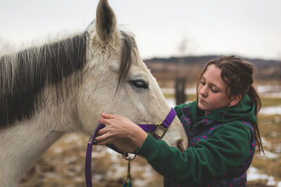 Teen girl putting halter on white horse