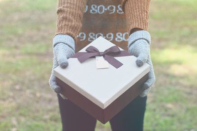 Midsection of woman giving gift box while standing at park