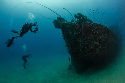 People scuba diving by shipwreck in sea