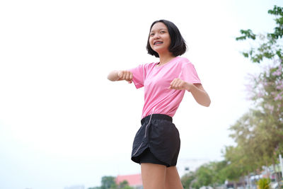 Low angle view of smiling teenage girl looking away while standing against clear sky