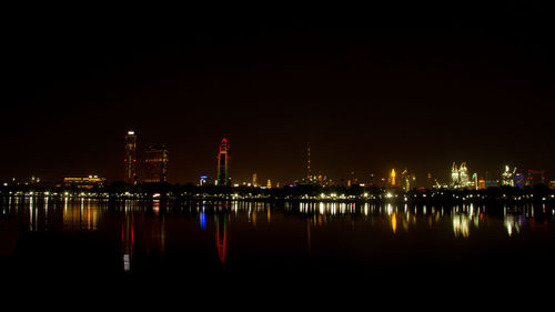 Illuminated buildings by river against clear sky at night