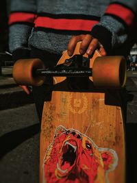 Midsection of man holding skateboard in city during sunny day