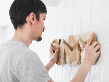 A young man hangs a wooden hanger on the wall in the bathroom.