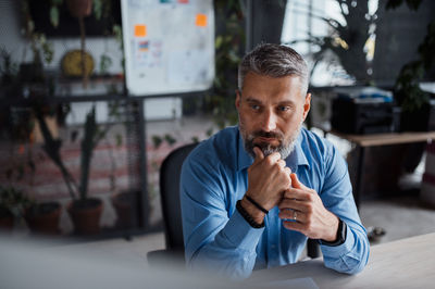 Thoughtful man working at contemporary office, watching computer, sitting on comfy chair