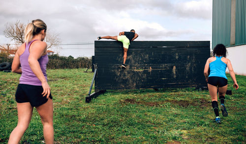 Rear view of friends climbing wooden wall while exercising outdoors