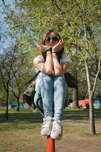 Portrait of young woman sitting on railing in park during sunny day