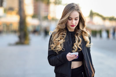 Beautiful young woman using mobile phone while standing in city