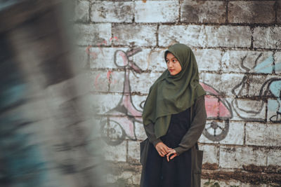 Portrait of young woman standing against wall