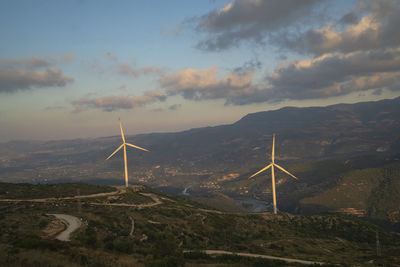 Wind turbines on mountain against sky during sunset