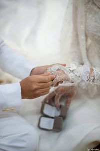 Midsection of groom putting ring in bride finger