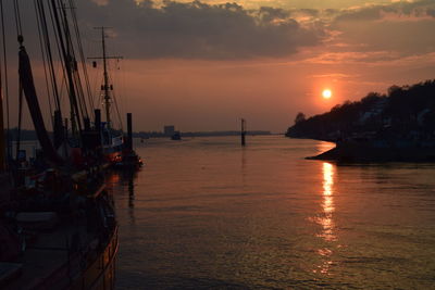 Sailboats moored in sea against sky during sunset