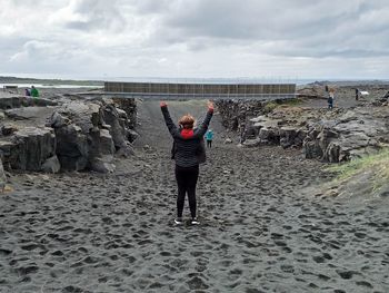 Rear view of women standing on rock at beach against sky