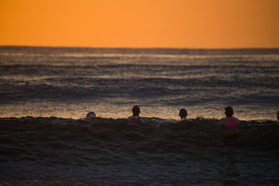 Friends swimming in sea against sky during sunset