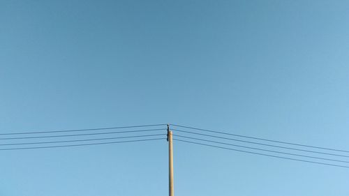 Low angle view of electricity pylon against clear blue sky