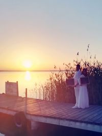 Rear view of couple standing against sea during sunset