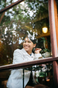 Portrait of a smiling young woman seen through window