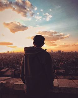 Rear view of man standing by buildings against sky during sunset