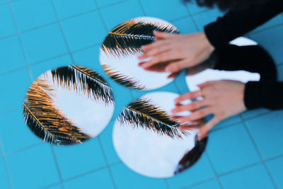 Cropped hands touching mirrors with reflection of palm trees