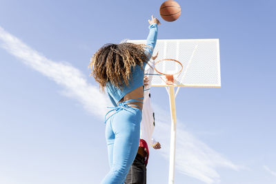 Female friend shooting in basketball hoop while playing on sports court