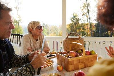 Mature man cutting apple while cheerful woman looking away on porch