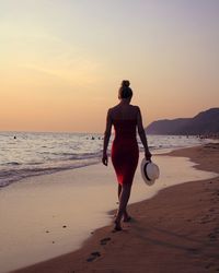 Rear view of young woman walking on shore at beach during sunset