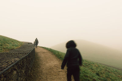 Rear view of people walking on mountain against sky during foggy weather